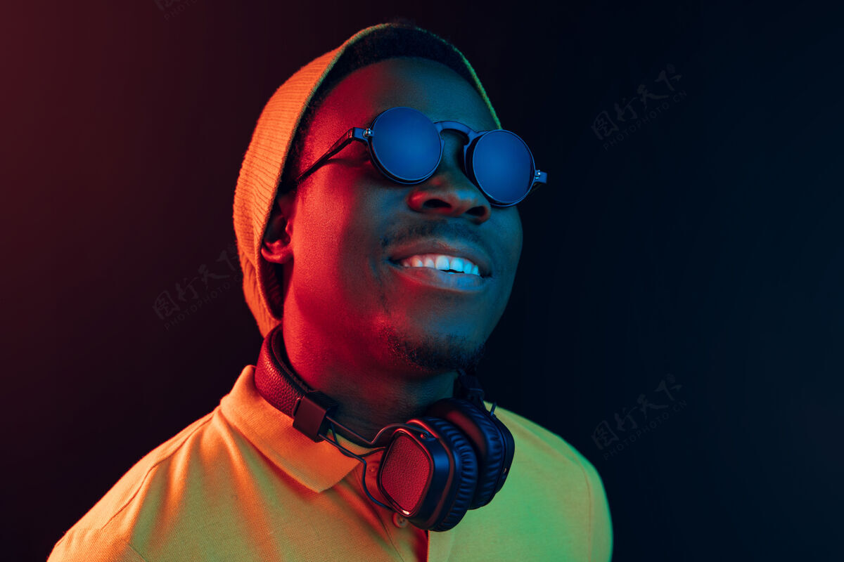 享受年轻帅气快乐的潮人在霓虹灯下的黑色演播室里戴着耳机听音乐说唱微笑耳机