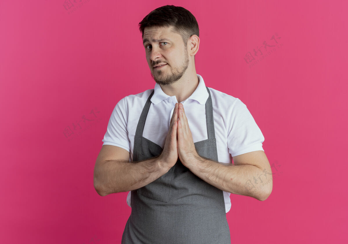 手围着围裙的理发师手挽着手 站在粉色的墙上 像是在祈祷或乞求 带着希望的表情站着理发师喜欢