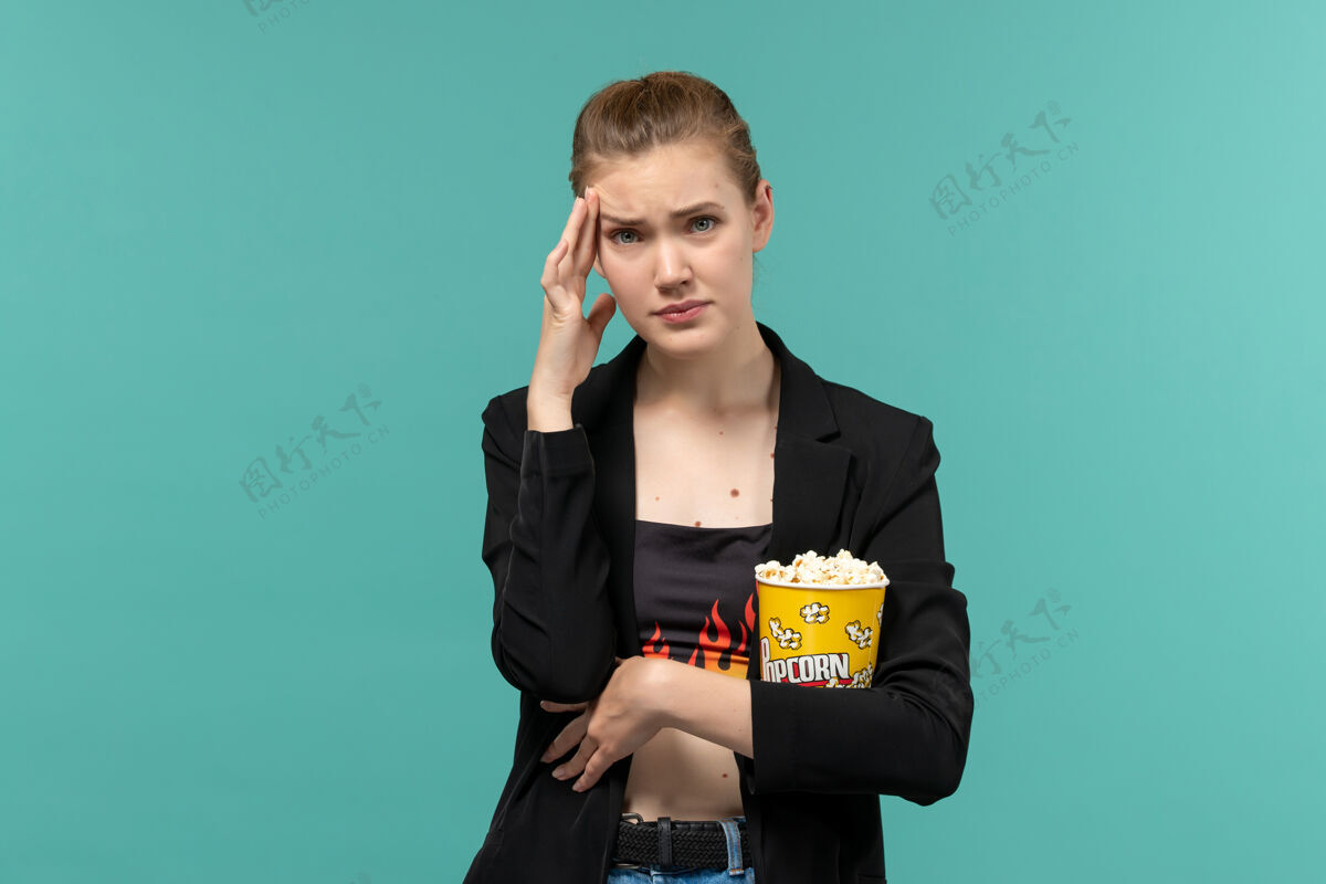 看正面图年轻女性手持爆米花包在蓝色表面看电影抱着秘书年轻的女性