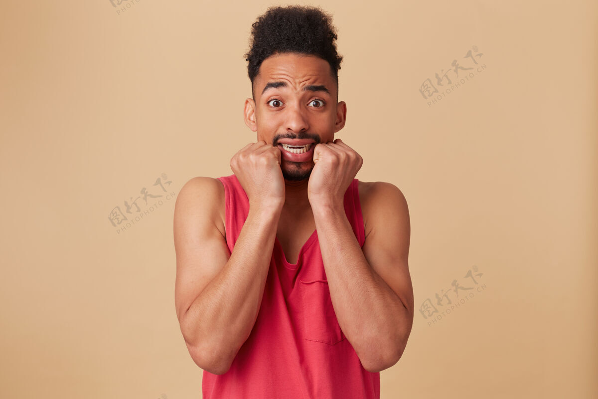 孤独惊恐的非洲裔美国男性的肖像 非洲发型和胡须穿着红色背心惊恐的 害怕的粉彩米色墙壁害怕拳头酷