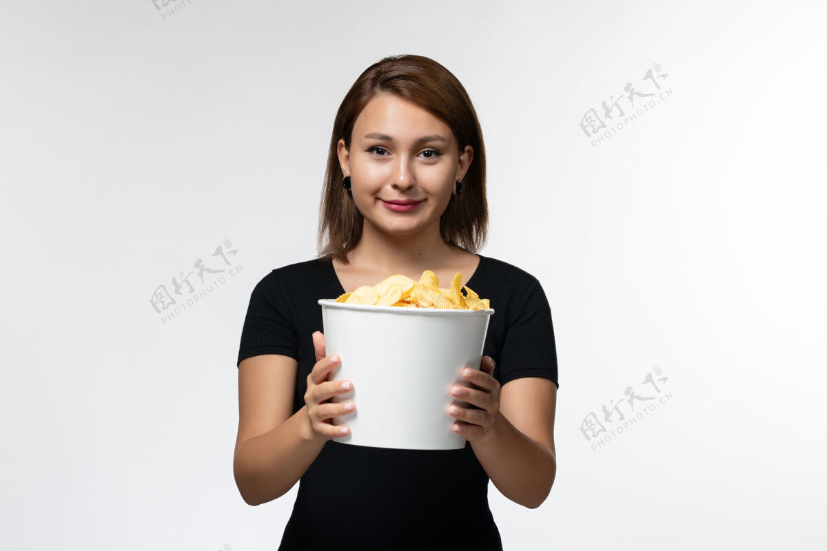 抱着正面图年轻的女性拿着篮子和薯片 在浅白的表面上微笑着看电影孤独浅白色电影