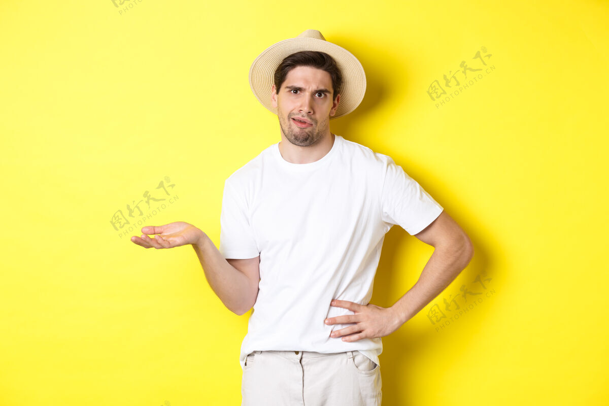 男人旅游和避暑的概念年轻的怀疑游客抱怨 看判断 站在黄色背景帽子节日工作室