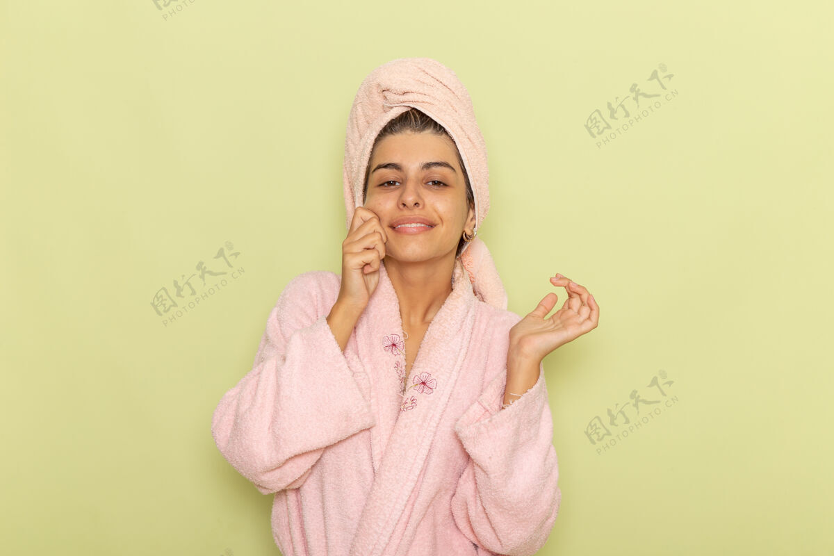 年轻女性正面图穿着粉红色浴袍的年轻女性在绿色的桌子上摆姿势微笑睡衣姿势前面
