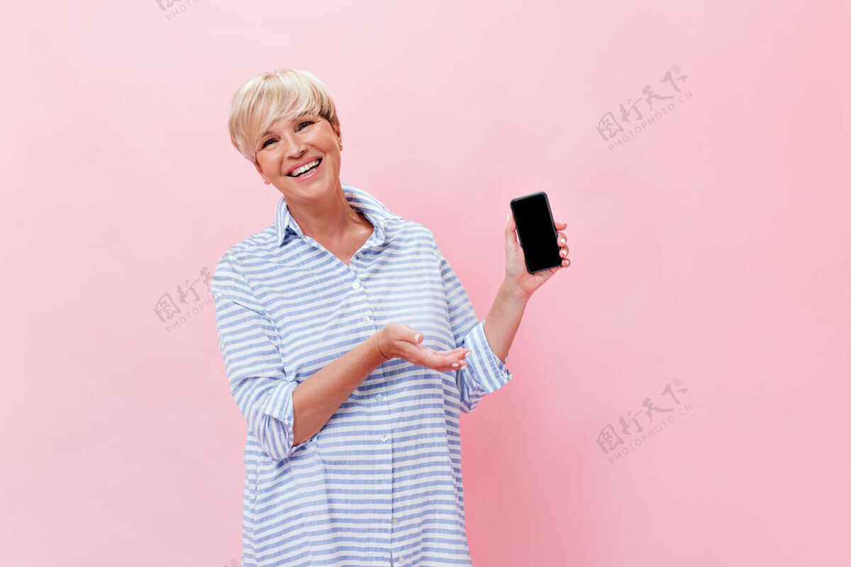 岁身着蓝色套装的金发女人在粉色背景上展示智能手机微笑女士脸