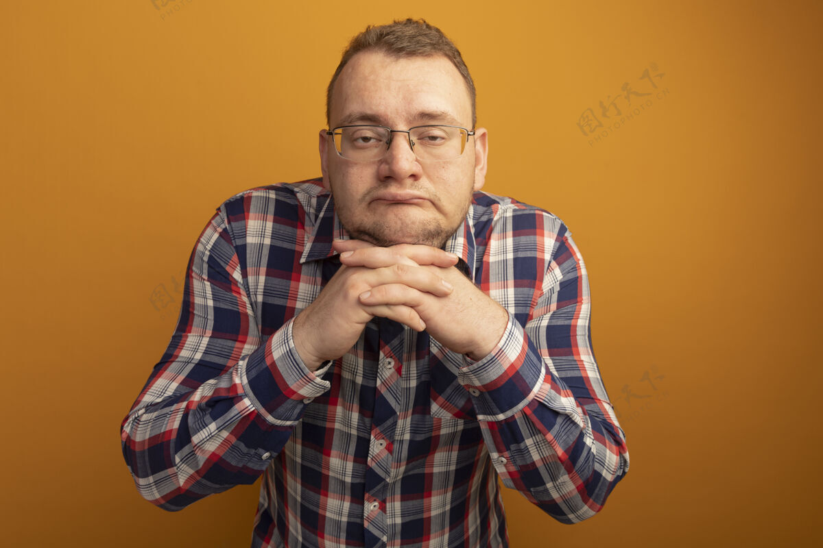 男人一个戴着眼镜 穿着格子衬衫的男人站在橘色的墙上又累又无聊检查站着眼镜