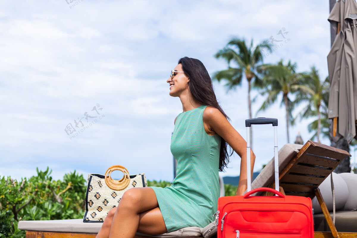 服装快乐的白种人漂亮的长发优雅的旅游女人在酒店外面穿着红色的手提箱时尚旅游女人