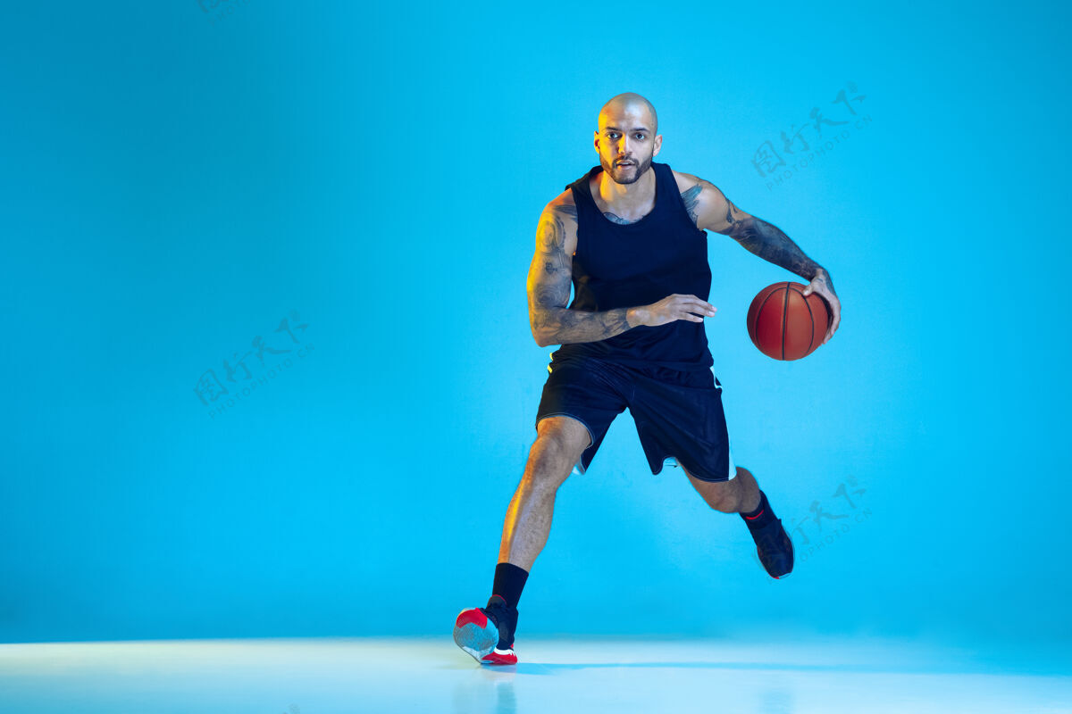 运动员年轻的篮球队员穿着运动服训练 在运动中练习 在霓虹灯下的蓝色背景下孤立运动运动的概念 运动 活力和活力 健康的生活方式健康篮球游戏