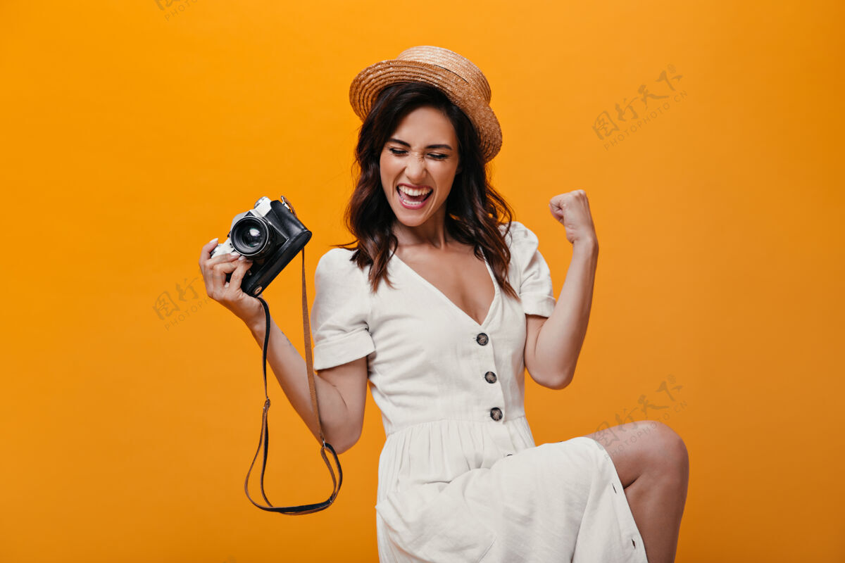 老式相机穿着白色连衣裙的酷女孩在橙色背景上快乐地摆着姿势 手里拿着复古相机梦幻衣服站立