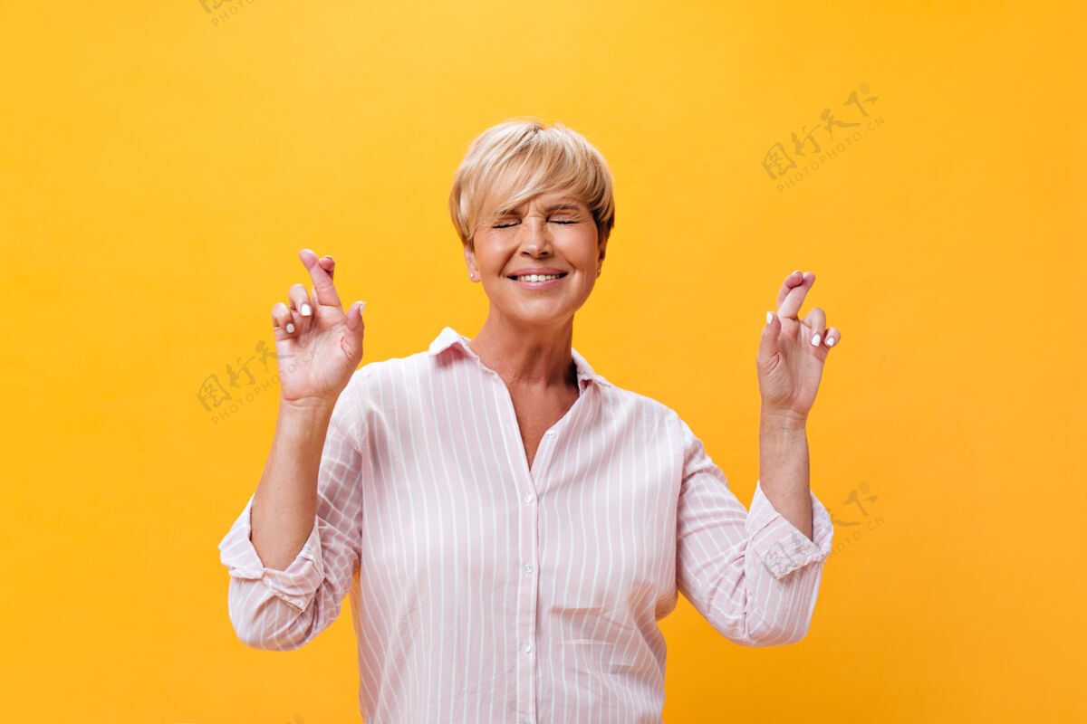 成熟身着粉色套装的快乐女士在孤立的背景上交叉手指健康老年年