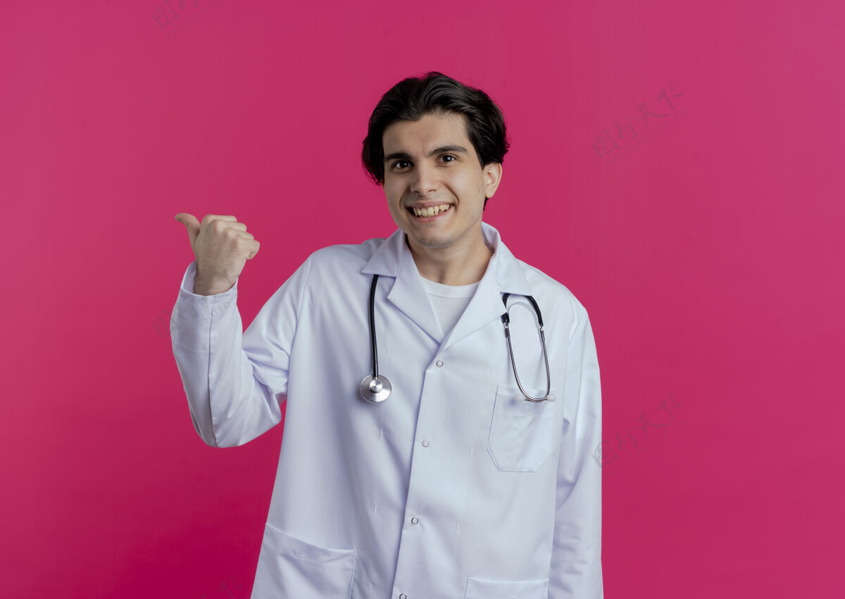 听诊器面带微笑的年轻男医生穿着医用长袍 听诊器指着身后隔离的粉红色墙上有复印空间年轻看穿