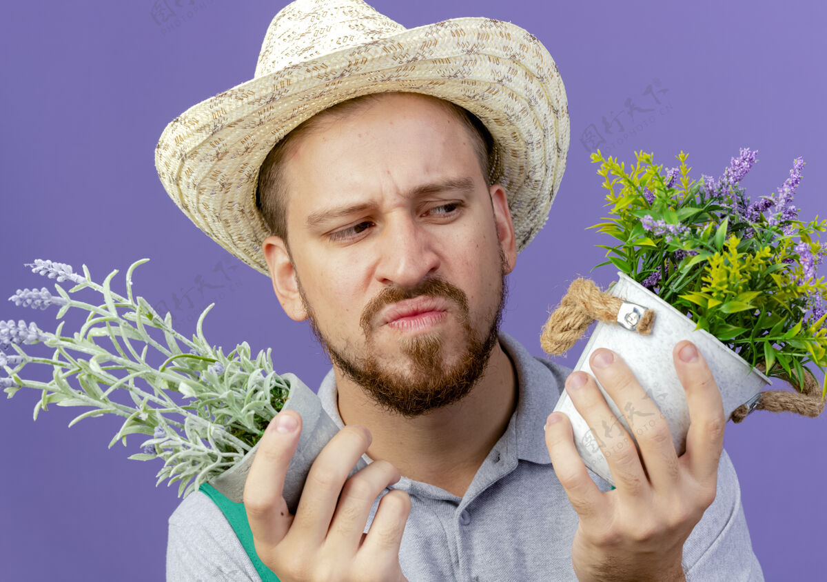 迷茫特写镜头中困惑年轻英俊的斯拉夫园丁身穿制服 戴着帽子 看着紫色墙上孤立的花盆风景特写帽子