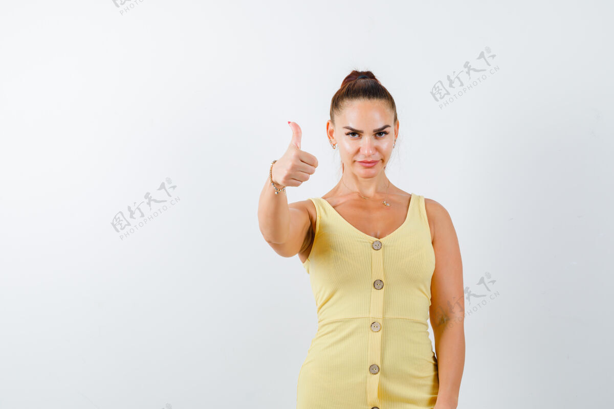 自信身着黄色连衣裙的年轻女士竖起大拇指 看上去自信满满的正面照片微笑姿势人物