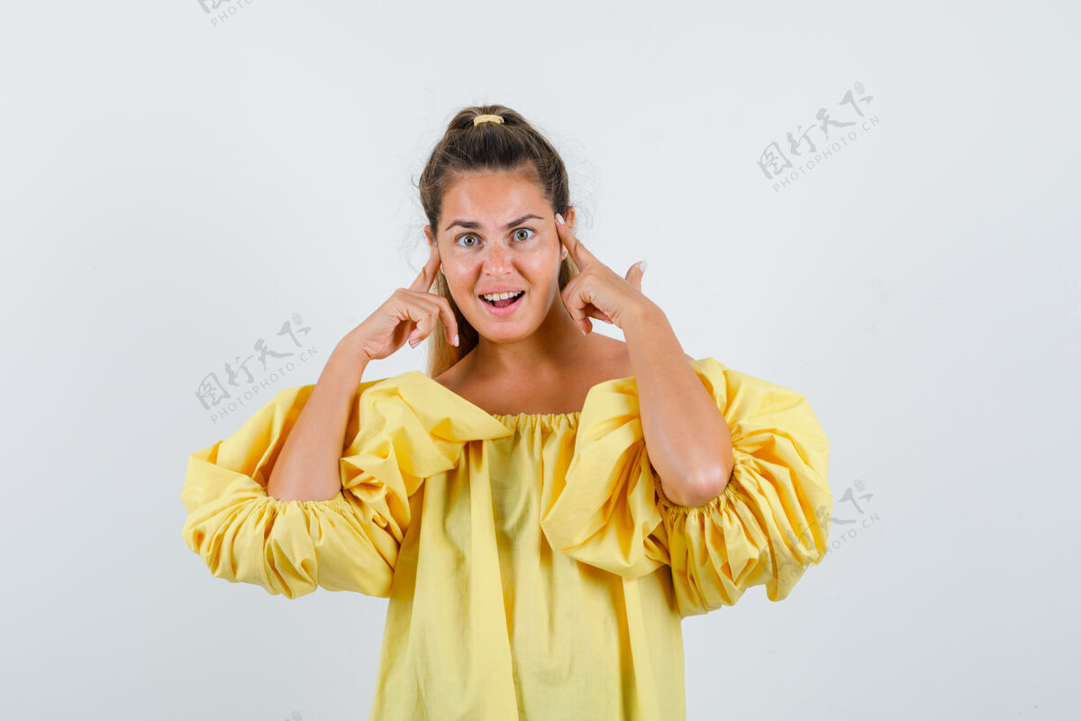 衣服穿着黄色连衣裙的年轻女士手指放在头上 看起来很高兴 正对着前方女人自然黄色