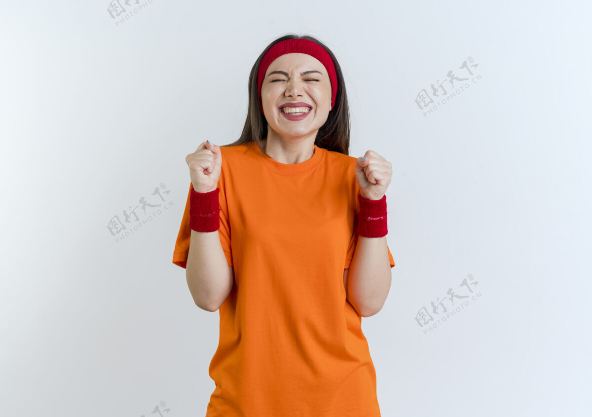 运动快乐的年轻运动女性戴着头带和腕带 闭着眼睛做着“是”的手势 隔离在白色墙壁上 留有复制空间欢乐头带女人