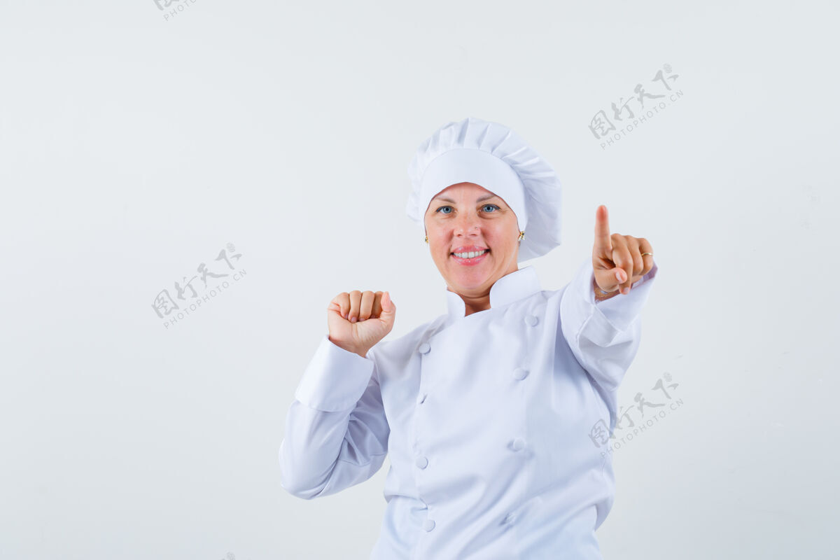 欢乐女厨师指着前面 同时展示她的拳头在白色制服粉色嘴唇脸