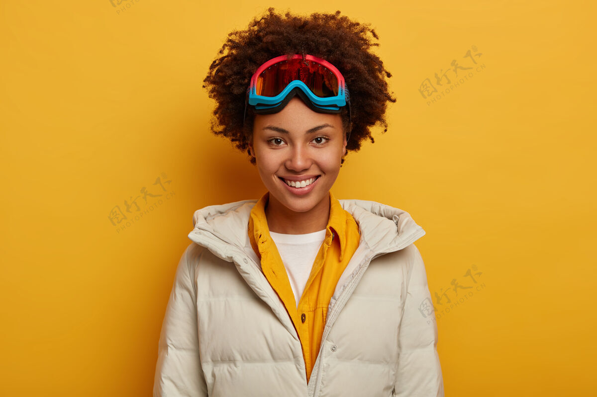 雪运动度假 旅游生活方式和冬季探险的概念快乐的非洲妇女牙齿微笑 滑雪板在山上 穿着滑雪护目镜和白色羽绒服女性面具明亮