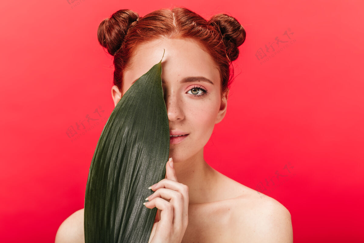 皮肤迷人的姜女与绿叶合影摄影棚拍摄的迷人的年轻女士与植物隔离在红色背景上微笑自然红发