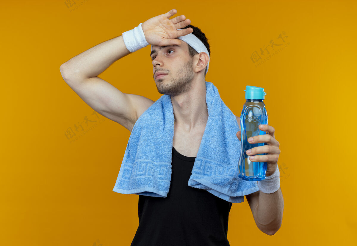 毛巾戴着头巾 脖子上围着毛巾 手里拿着一瓶水的年轻运动型男子 在橘子汁上锻炼后 又累又累男人锻炼运动