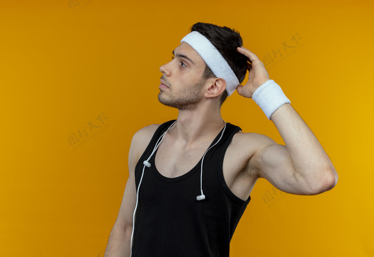 看戴着头巾的年轻人站在橘色的墙上 困惑地向一边看 挠头运动年轻男人