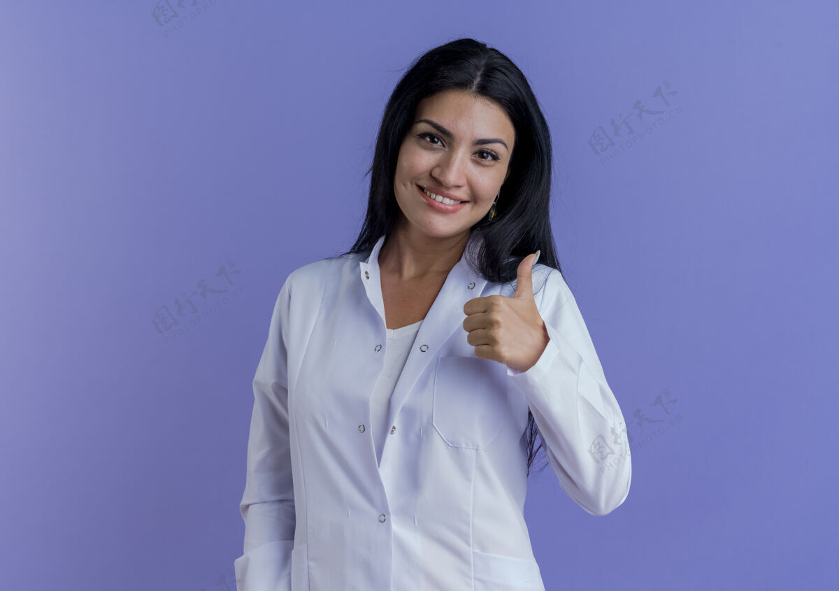 女性面带微笑的年轻女医生穿着医用长袍 抬起大拇指看年轻向上