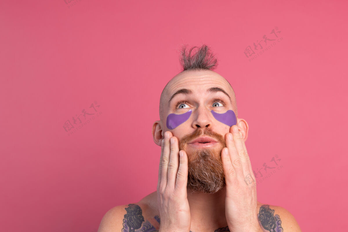 清洁欧洲帅哥留着胡子纹身上身的男人戴着紫色眼罩对着镜头摆粉红色的姿势贴片空虚房子