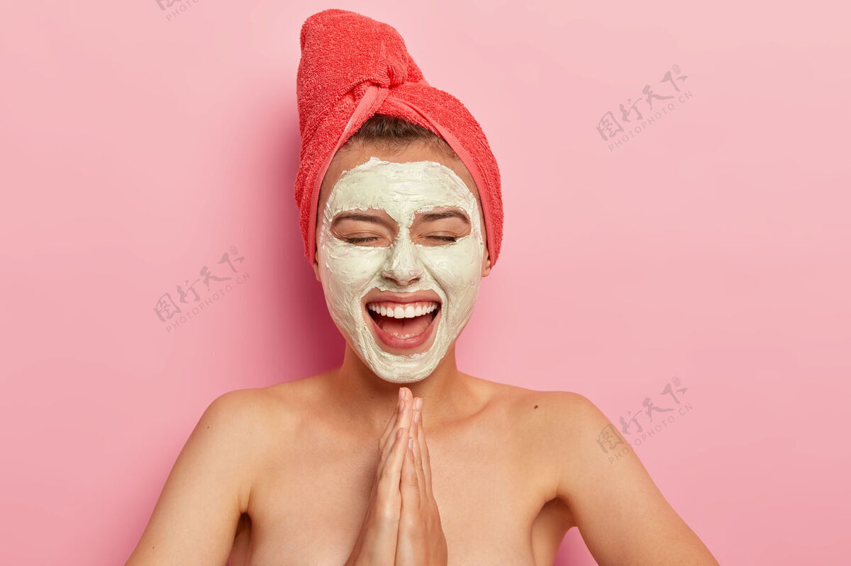 祈祷快乐的女性在祈祷姿势中保持手掌 宽泛地微笑 戴上面罩复活节 在家里玩得开心 裸露的肩膀裸露在粉红色墙壁上放松美容室内