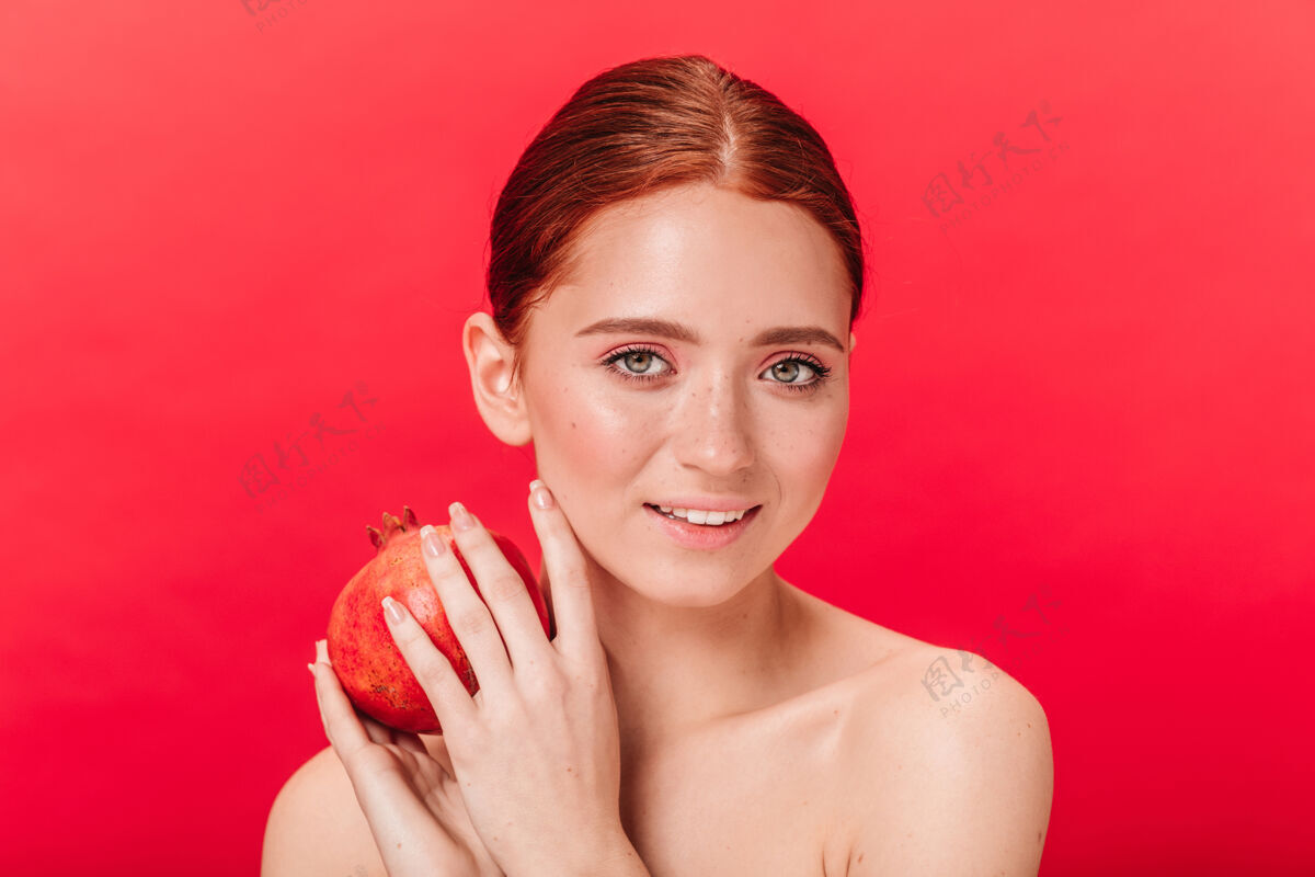 生姜迷人的女孩抱着石榴石 带着温柔的微笑摄影棚拍摄的令人惊叹的姜汁女士 红色背景上有水果自然微笑裸体