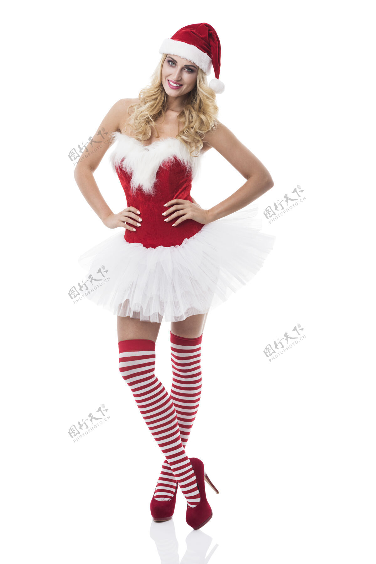 高跟鞋穿着圣诞老人服装的性感女人在白墙上摆姿势圣诞老人肖像连衣裙