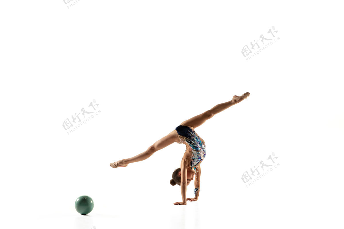 体操一个柔韧的小女孩被隔离在白色的墙上穿着鲜艳的紧身衣的艺术体操艺术家的小女模优雅的动作 动作和运动用球做练习紧身衣闪光艺术家