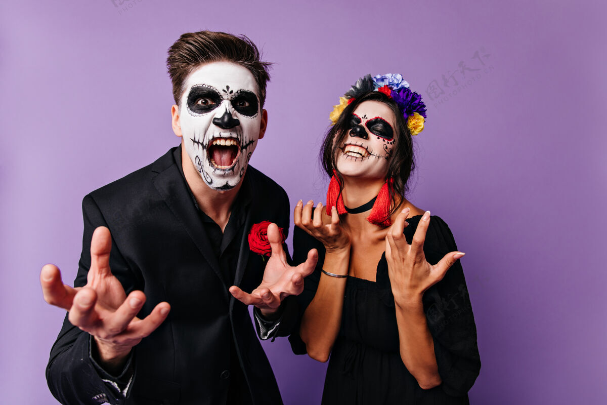 浪漫戴着骷髅面具的愤怒的男孩和女孩情绪化地摆姿势 想要展示他们的伟大黑发墨西哥夫妇的画像墨西哥节日骷髅
