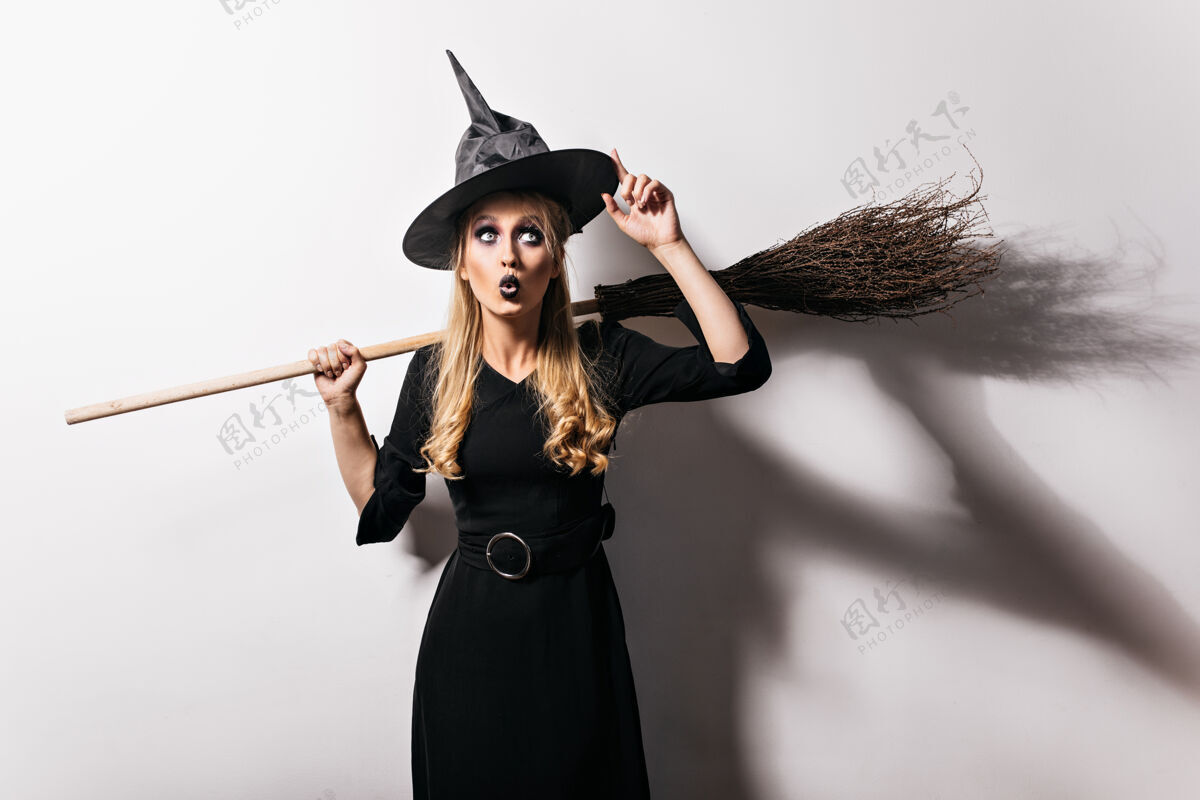 服装惊艳的金发女巫抚摸着她的魔法帽子迷人的吸血鬼女孩准备在万圣节狂欢节传统优雅恐惧