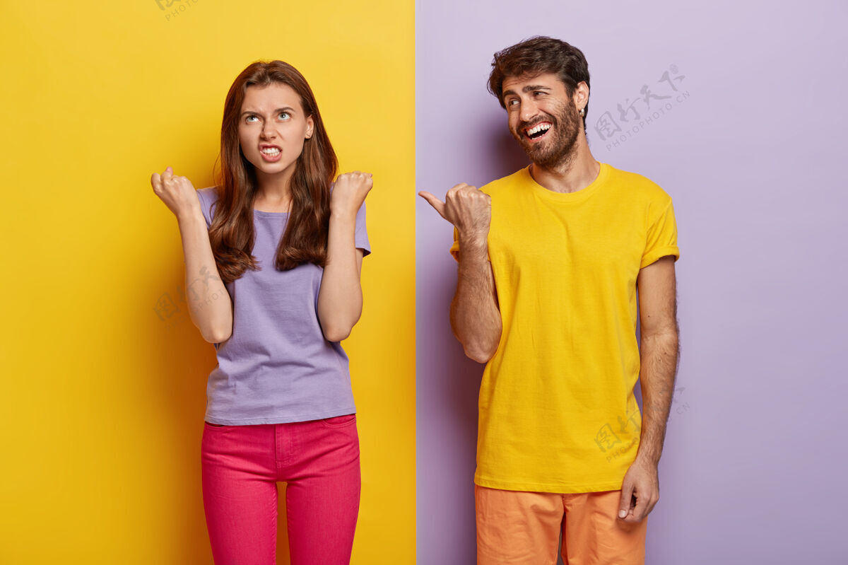 男人高兴的家伙玩得很开心 穿着亮黄色的t恤 用拇指指着生气地握拳的女朋友绝望休闲情侣