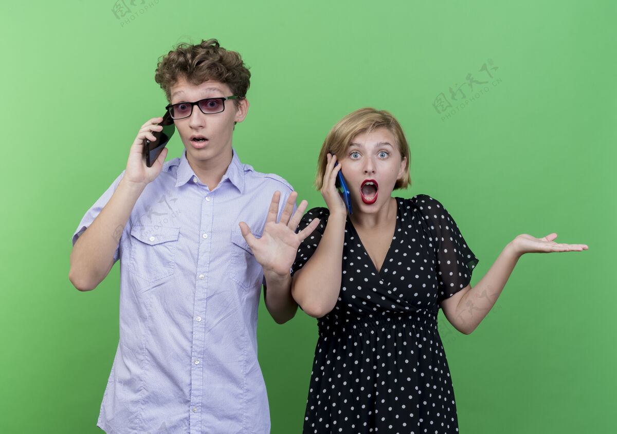 聊天一对年轻漂亮的夫妇站在绿色的墙壁上 一对男女正在用手机交谈 看上去迷茫而不确定情侣困惑男人