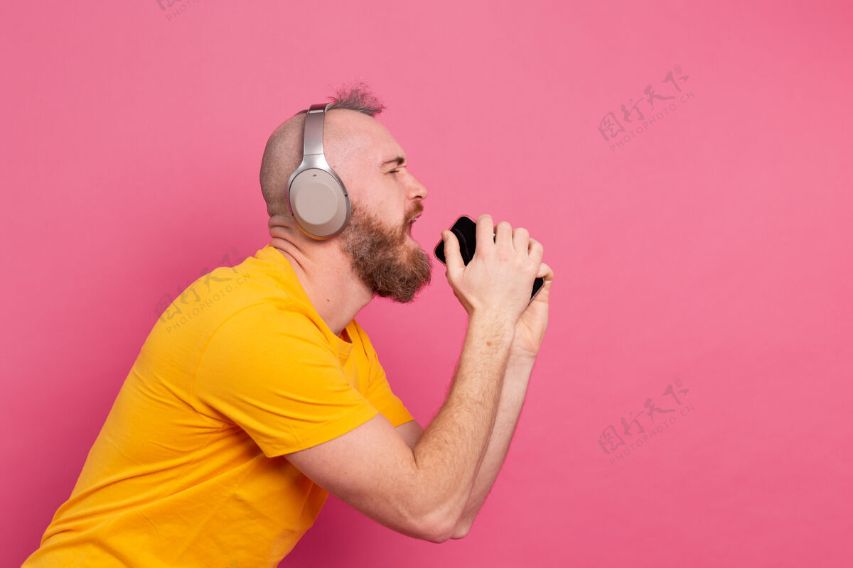 家伙帅哥带着手机耳机在粉色背景上随意唱歌听力休闲休闲