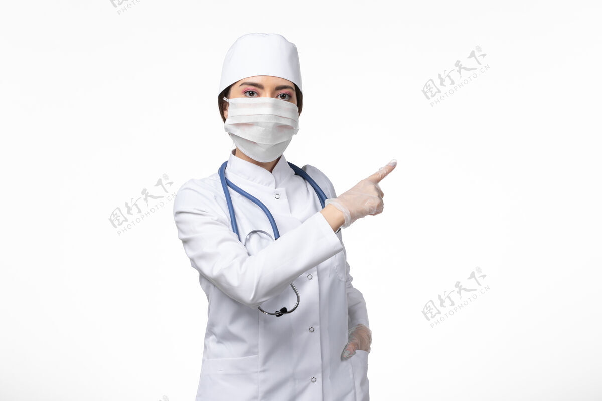 专业正面图女医生穿着白色无菌医疗服 戴着口罩因冠状病毒-摆在淡白色墙壁上病毒冠状病毒-大流行性疾病面罩疾病正面