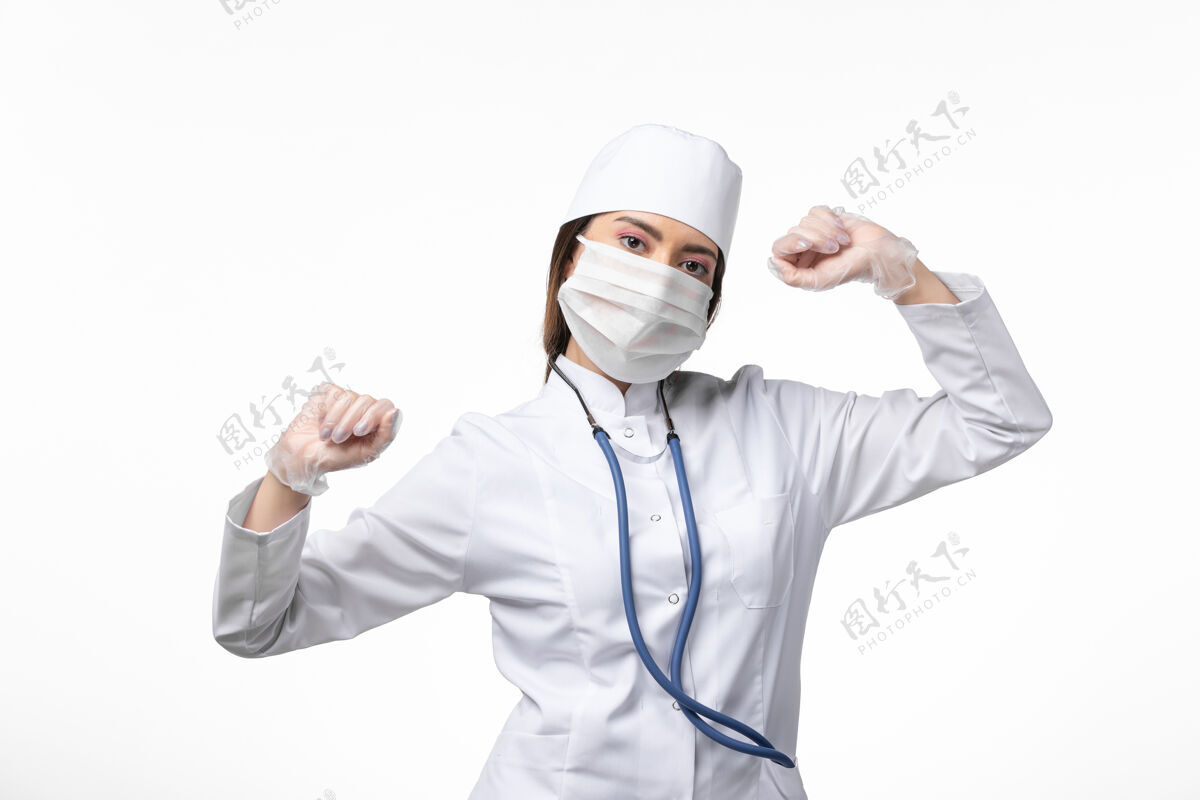 冠状病毒正面图女医生穿着白色医疗服 带着口罩因冠状病毒在白墙上微微舞动疾病医学病毒大流行covid-医疗医生套装