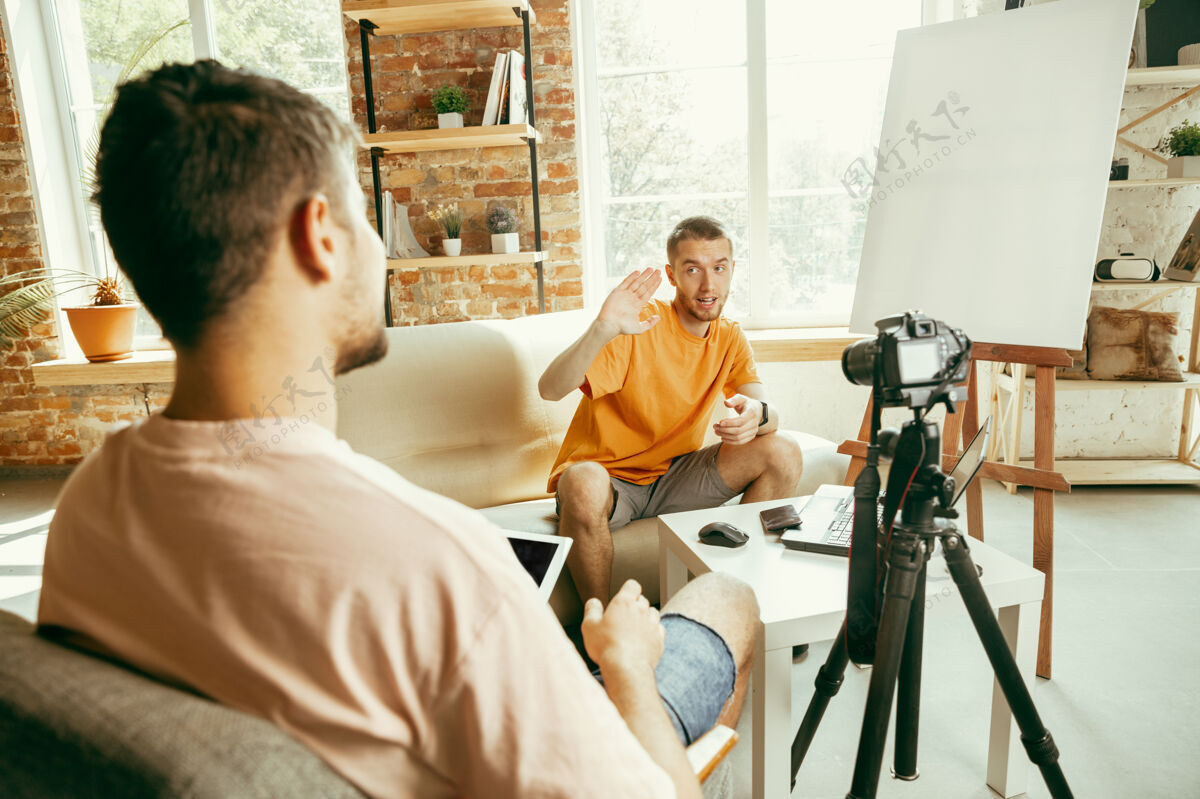 技术两位年轻的白人男性博主穿着休闲服 用专业设备或摄像机在家里录制视频采访采访小工具广播