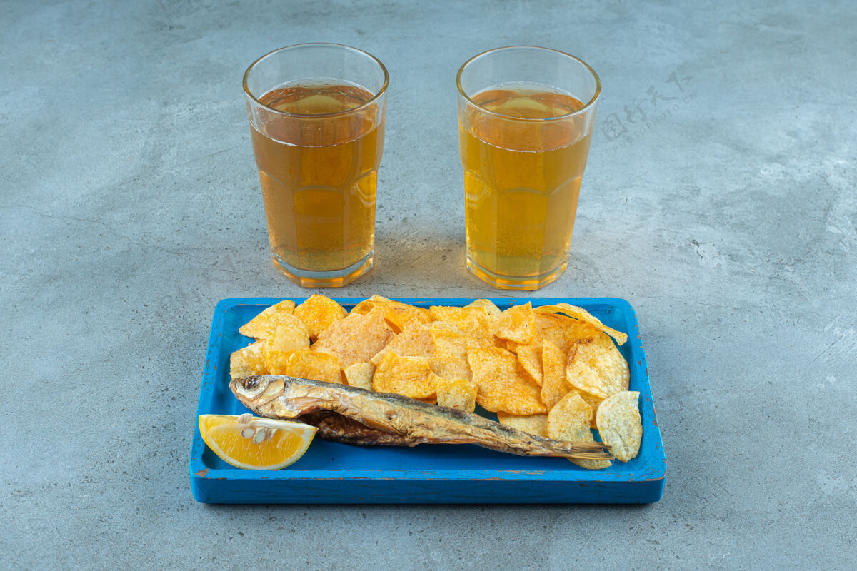 啤酒木盘上的薯条和鱼 旁边是两杯大理石啤酒玻璃杯美味啤酒