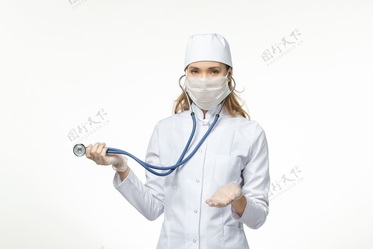 女性正面图女医生穿着白色医疗服 戴着无菌口罩 由于冠状病毒使用听诊器在白色办公桌上患病 冠状病毒-大流行性疾病使用到期正面
