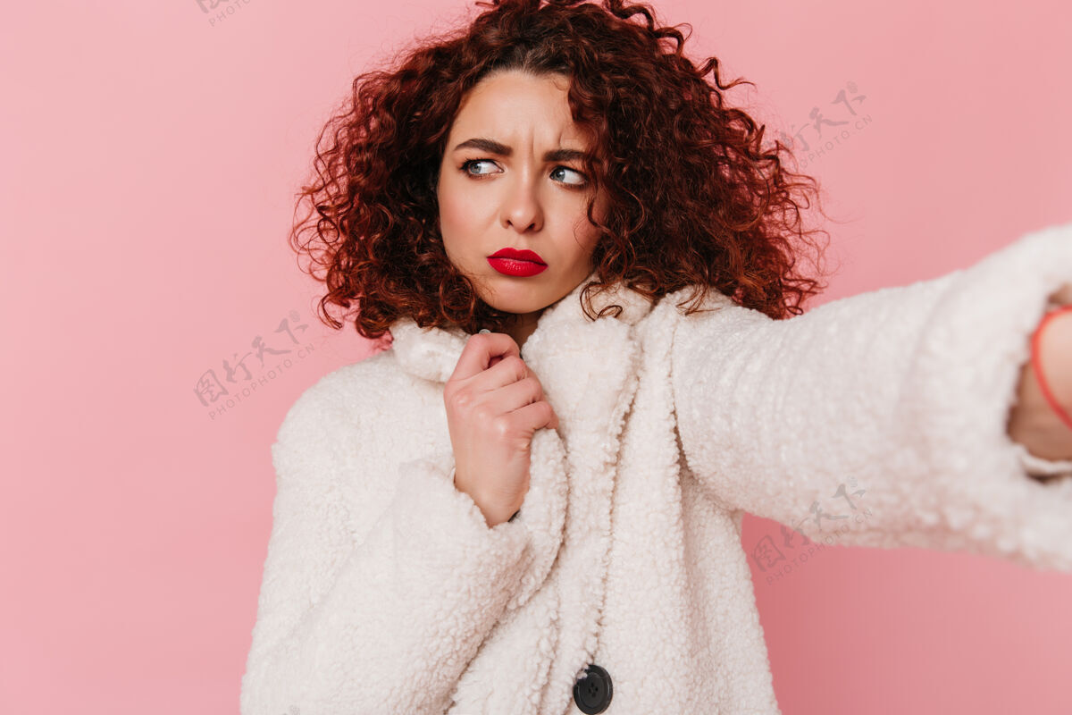 优雅一个活泼的卷发女孩 红唇 穿着白色羊毛外套 在粉色的隔离空间里自拍身体积极魅力