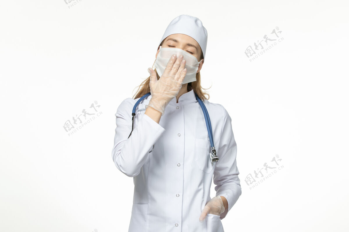 女性正面图女医生穿着医疗服戴口罩因冠状病毒打呵欠白墙病病毒冠状病毒-大流行性疾病专业人打哈欠