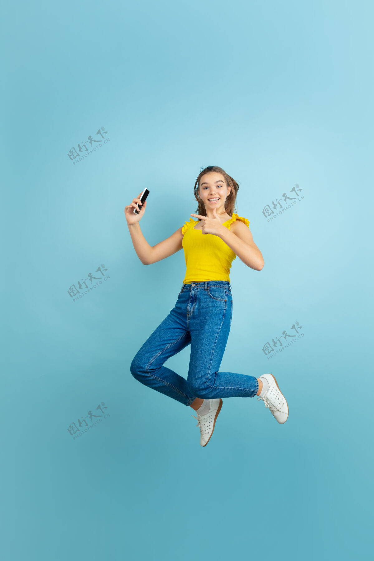 青少年拿着智能手机跳高蓝色的高加索少女肖像人物年轻人教育