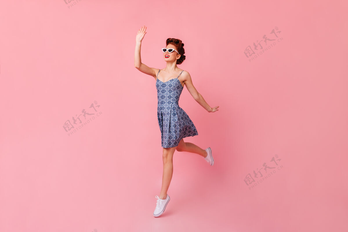 欧式戴着太阳镜的漂亮女孩挥舞着手摄影棚拍摄了一个在粉色空间跳跃的快乐的小姑娘爱情情感淑女