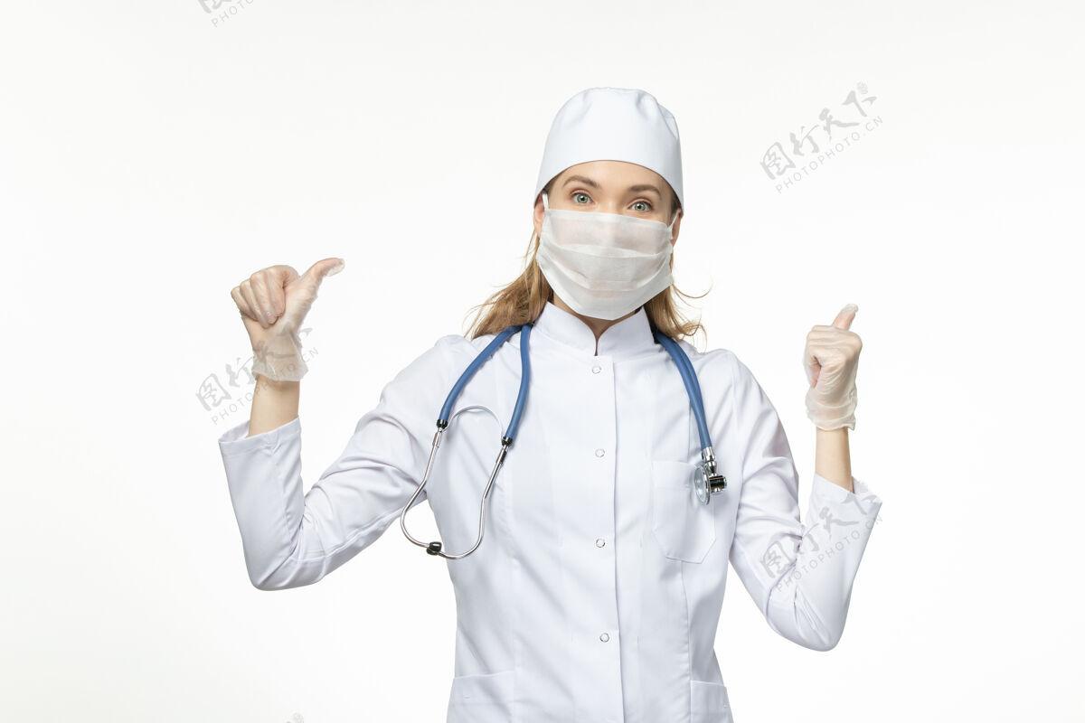 专业人员正面图女医生穿着医疗服戴着口罩和手套因白色办公桌上的冠状病毒病病毒冠状病毒-大流行性疾病正面听诊器办公桌