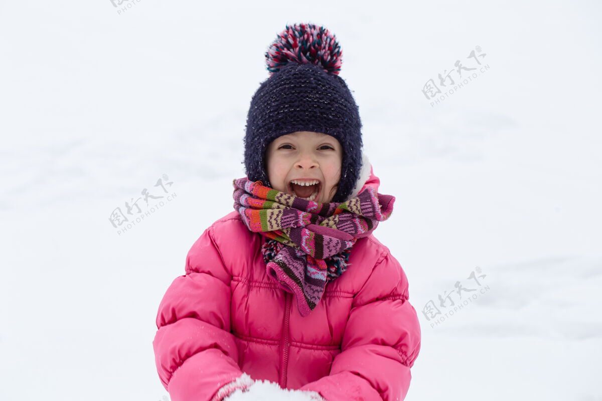 下雪一个穿着粉色夹克 戴着帽子的可爱小女孩正在雪地里玩耍冬季儿童娱乐理念寒冷下雪游戏