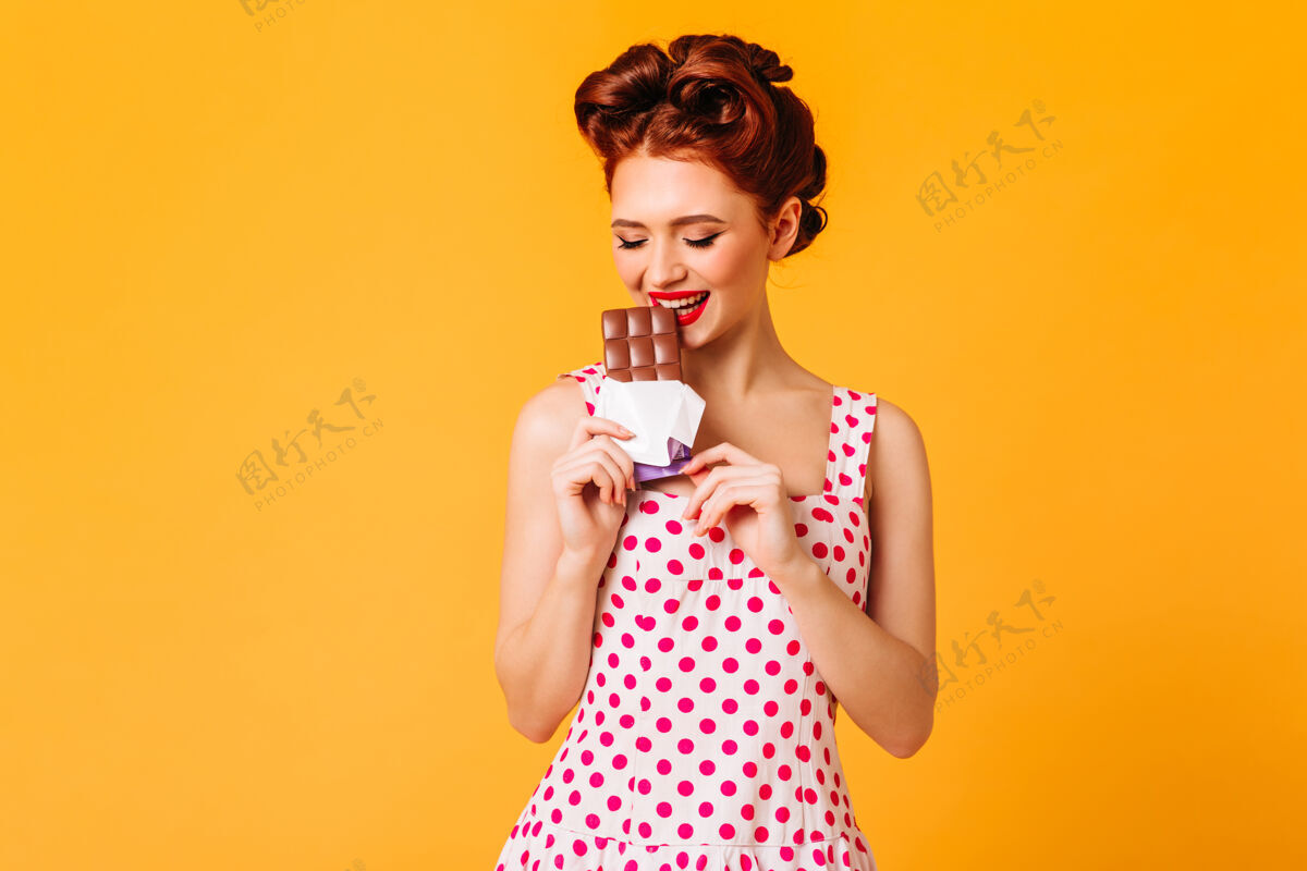 连衣裙穿着圆点裙的漂亮女孩正在吃巧克力黄色空间里姜红色系腰女士正在享用甜点的摄影棚镜头表达吃东西年轻人