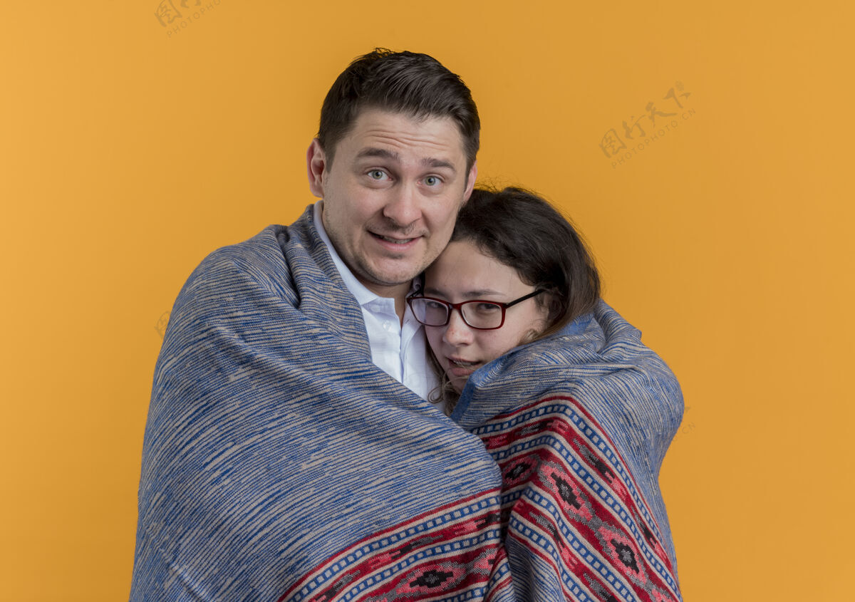 女朋友一对幸福的年轻人 用温暖的毯子盖住他冻坏了的女友 站在橙色的墙上情侣年轻毯子