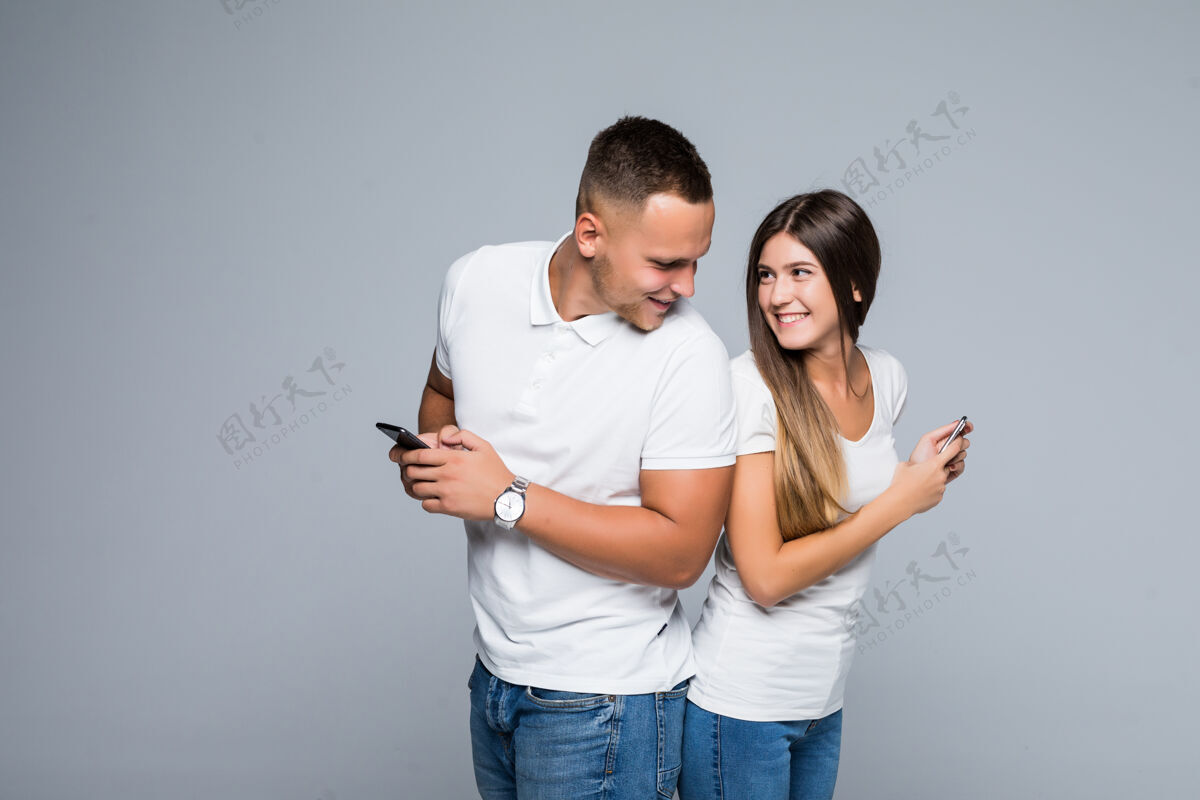 商店一对男女年轻夫妇手拿手机站在灰色的背景上牛仔裤空白休闲