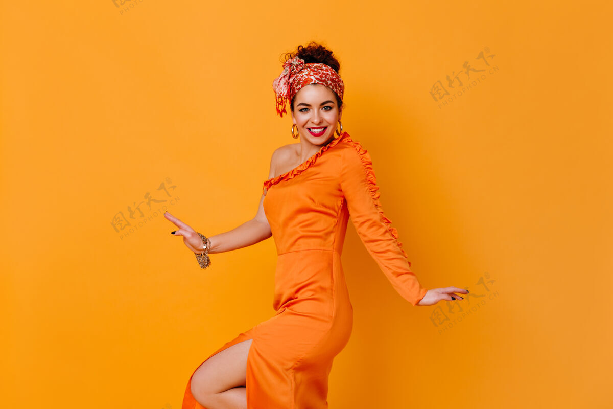 姿势一位戴着不寻常头带 穿着开叉缎子连衣裙的女士在橙色的空间里微笑着长连衣裙现代完美