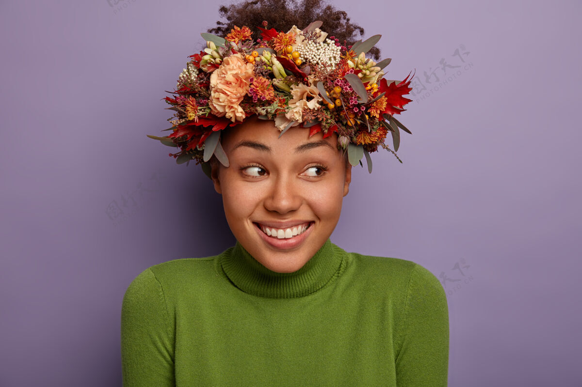 旁边迷人的快乐女性有着自然的美丽 没有化妆 戴着秋天的植物花环 高兴地看着旁边 感到高兴 戴着绿色的马球衫 在室内做模特室内秋天喜悦